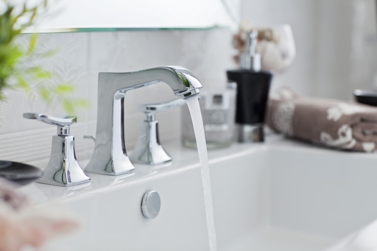 Water flowing from modern bathroom faucet into sink.