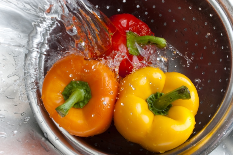 Washing colorful peppers in colander.